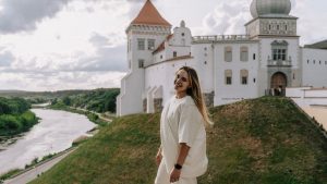 A woman enjoys a sunny day by a historic castle, with scenic river view.